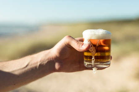 Celebrating life, man holding glass of lager beer at the beachの写真素材