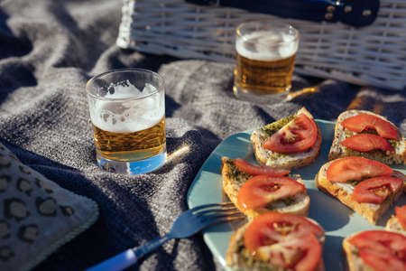 Summer picnic in nature with tomato and pesto sandwiches, and beer in glassesの写真素材