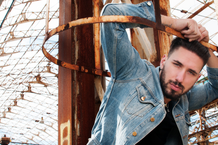 young man on a ladder with denim jacket, black shirt and pants of low waist jeans. metropolitan background. Sunglasses in one hand. a hand through his hair.の写真素材