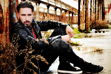young man sitting.  metropolitan background. Wearing a black leather jacket and a red shirt black pantsの写真素材