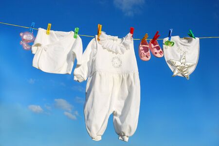 baby clothes and accessories hanging on clothesline against blue skyの写真素材