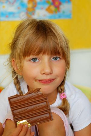 little girl with blonde plaits eating big  bar of chocolateの写真素材
