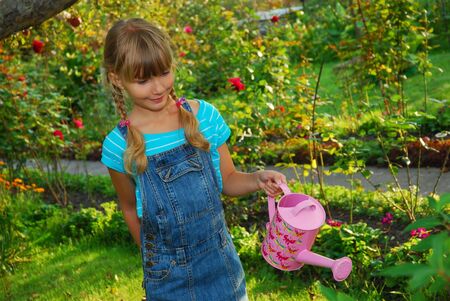 young girl  watering flowers in the garden with pink canの写真素材