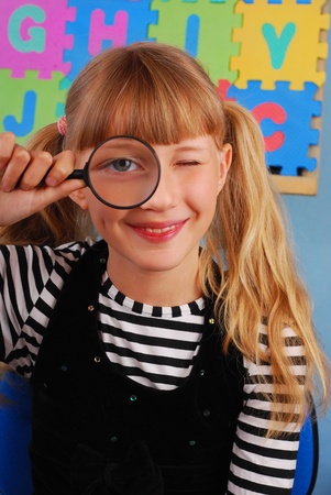 schoolgirl in the classroom in funny pose with magnifying glassの写真素材