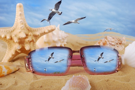sunglasses lying on the beach with reflection of flying seagullsの写真素材
