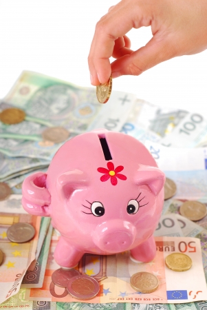 hand  throwing the coin into pink piggy bank standing on banknotes backgroundの写真素材