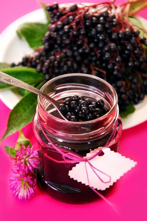 jar of homemade elderberry confiture and fresh fruits on pink backgroundの写真素材