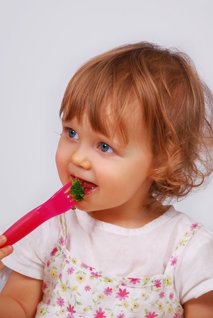 little baby girl eating broccoli by herself using a plastic forkの写真素材