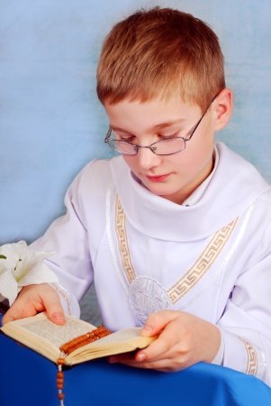 young boy in white alb going to the first holy communion and praying with prayer bookの写真素材