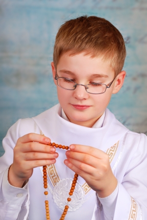 young boy going to the first holy communion in white alb praying with a rosary の写真素材