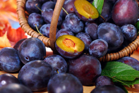  fresh plums falling out of wicker basket on wooden table