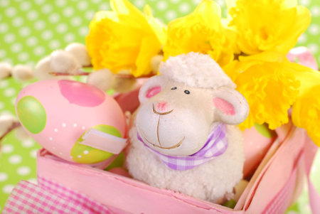 pink easter basket with eggs and funny sheep figurine on green dotted backgroundの写真素材