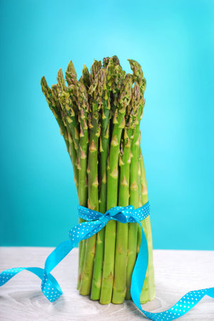 bunch of fresh green asparagus standing against blue background の写真素材