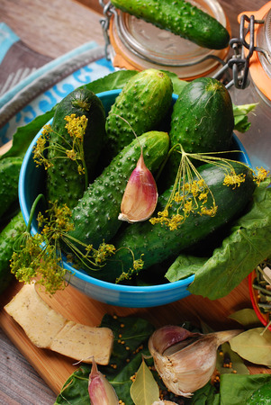 bowl of fresh cucumbers and ingredients for homemade gherkin on wooden backgroundの写真素材