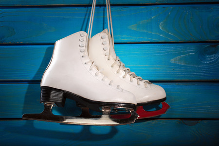 pair of white ice skates for girl hanging on blue wooden backgroundの写真素材