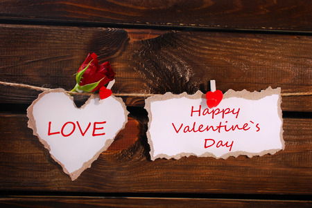 torn paper heart with red rose and card hanging on twine against wooden wallの写真素材