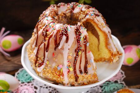 easter ring cake with icing ,chocolate glaze and colorful sprinkles on wooden background