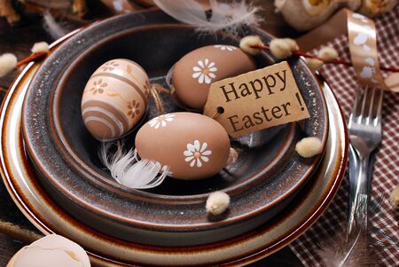 easter eggs and paper tag with greeting text in plate on rustic wooden table
