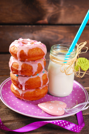 homemade donuts with pink icing and sprinkles on plate and bottle of milkの写真素材