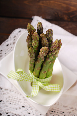 bunch of fresh green asparagus tied with ribbon and standing in white bowlの写真素材