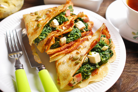 plate of spinach ,bacon and feta filled pancakes on wooden tableの写真素材