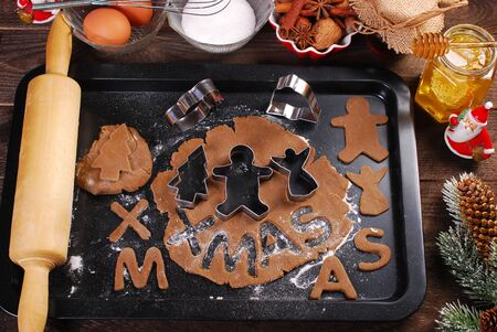 christmas gingerbread dough and cookie cutters on black tray with ingredients and utensils