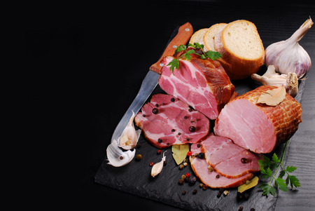 pieces of delicious homemade smoked pork ham with spices and bread on black background and space for...