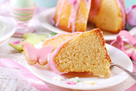 partly sliced easter ring cake with pink icing and colorful butterfly shaped sugar sprinkles on...