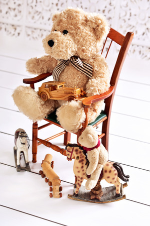 old teddy bear sitting on wooden chair with his toysの写真素材