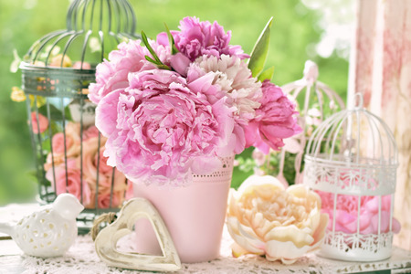 pink peony bunch in vase and vintage bird cages on the table in the gardenの写真素材