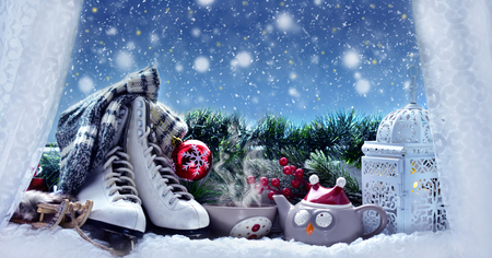 winter snowy evening with cup of hot tea,old figure skates and vintage style lantern and Christmas decoration on window sillの写真素材