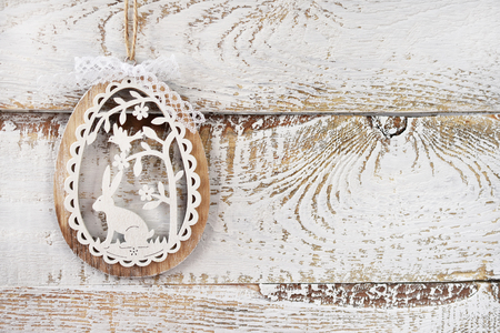 white wooden background with  openwork easter decoration in egg shape with rabbit and floral patternの写真素材