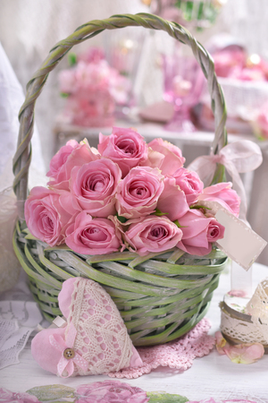 romantic bunch of pink roses with paper tag in green wicker basket in shabby chic style interiorの写真素材