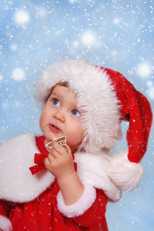 little girl in santa hat eating gingerbread cookie on christmas snowy dayの写真素材