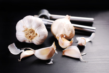 fresh garlic bulbs and cloves with presser lying on black background