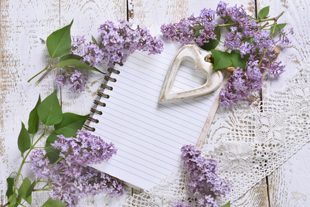 romantic style flat lay with purple lilac, a heart and a notebook with space for own text on white wooden backgroundの写真素材