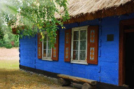 traditional village cottage with thatched roof and walls painted on blue with wooden shuttersの写真素材