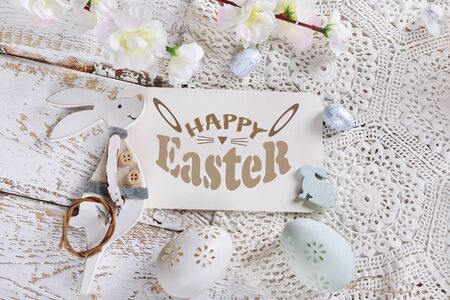 easter flat lay with greeting text, bunny figurine and eggs on white lace and wooden backgroundの写真素材