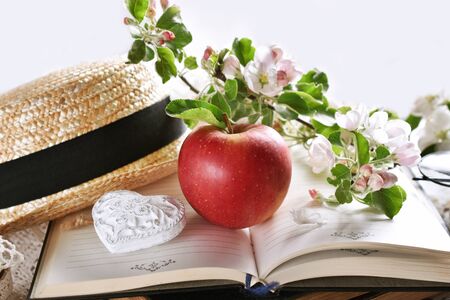 spring still life in romantic style with apple, blossom branches and straw hat on old booksの写真素材