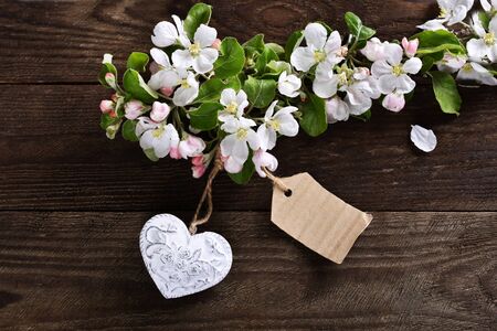 spring background with apple blossom branch on dark wooden table with a heart and a paper tag with...