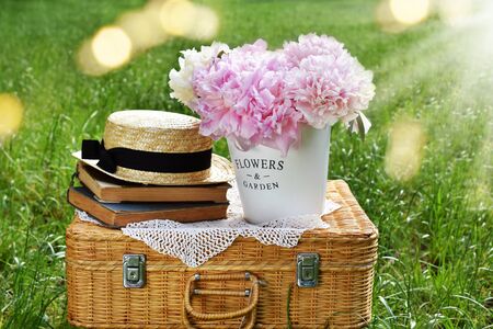 bunch of pink peonies in metal bucket standing on retro style picnic wicker basket on the grass in the gardenの写真素材