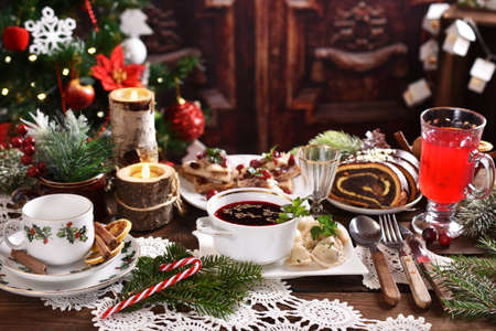 traditional in Poland Christmas Eve dishes with red borscht and dumplings, herring with cranberries and poppy seed roll cake on festive table in rustic styleの写真素材