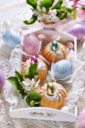 Easter mini ring cakes in white wooden tray, eggs and fresh spring flower decoration on festive...