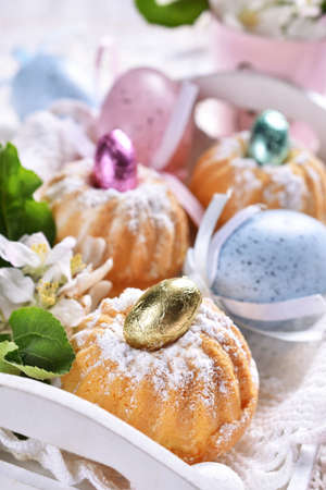 Easter mini ring cakes in white wooden tray, eggs and fresh spring flower decoration on festive...