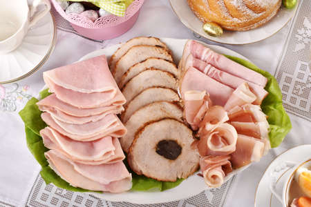 traditional Easter dishes with platter of cured meat and cakes on festive table in Poland