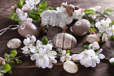 Easter background with a lamb figurine, colored eggs and spring apple tree blossoms on wooden table