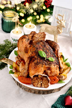 Roasted whole chicken with potatoes, mushrooms, tomatoes and garlic on Christmas table with festive decorations and white linen tableclothの写真素材
