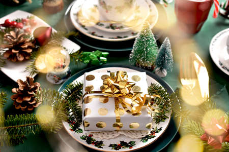 Christmas table setting with gift box on the plate, beautiful decors and green tableclothの写真素材