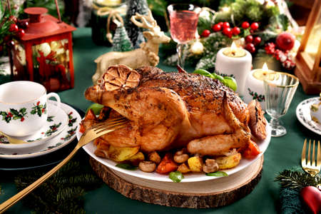 Roasted whole chicken with potatoes, mushrooms, tomatoes and garlic on Christmas table with festive decorations and green tableclothの写真素材