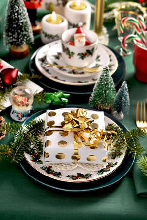 Christmas table setting with gift box on the plate, beautiful decors and green tableclothの写真素材